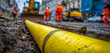 © AndiAzis - A yellow plastic water pipe lying on a construction site with workers and vehicles in the background