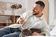 © Pixel-Shot - Handsome young man with mobile phone and cute cat sitting on bed in bedroom