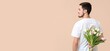 © Pixel-Shot - Handsome man hiding bouquet of beautiful flowers behind his back on beige background with space for text