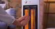 © Pixel-Shot - Young woman warming hands near electric heater in evening at home, closeup