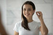 © fizkes - Daily hygiene. Head shot cheerful young woman stand in front of mirror gently clean ear with cotton bud swab remove dirt practice safe delicate self care routine at home enjoy morning bathroom ritual