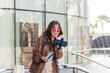 © sorapop - Asian woman enjoys shopping, people embrace fashion lifestyle with shopping bags, vlogging near modern mall, holding phone on stick, posing outside city building