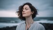 © Oleksandr - A woman with dark hair stands near the ocean, eyes closed, basking in the serenity. The tranquil scene suggests a moment of mindfulness & connection to nature.