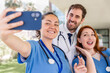 © StockMe - Medical professionals taking a team selfie, celebrating teamwork and healthcare dedication with smiles, capturing a joyful moment outside a modern hospital building
