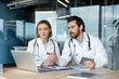 © Liubomir - Medical professionals working together at an office desk, discussing information on a laptop, a male doctor pointing at the screen while holding a digital tablet