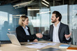 © Liubomir - Two smiling business professionals in a modern office shake hands across a desk, closing a partnership deal with paperwork, laptop and charts signaling successful collaboration and trust