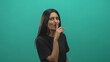 © Krakenimages.com - Woman pressing index finger to lips shushing in studio with teal backdrop and black shirt; playful secrecy.