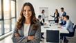 © infinite - Confident businesswoman smiling with crossed arms in modern office during team meeting, professional workplace environment, front view