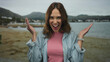 © Krakenimages.com - Hispanic woman joyfully expressing emotions at a beach with sea and mountains in the background, capturing a perfect blend of nature and human excitement.