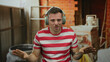 © Krakenimages.com - Man wearing headphones in striped shirt at construction site, expressing emotions with hand gestures showcasing tattoos on arm.