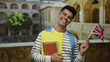 © Krakenimages.com - Young man holding british flag and folders in an old university courtyard setting, symbolizing education and international studies.
