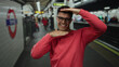 © Krakenimages.com - Young man wearing glasses making a framing gesture at a busy train station surrounded by commuters and bright lighting, capturing an urban scene.