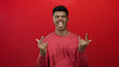 © Krakenimages.com - Man making playful hand gesture and sticking out tongue, wearing pink shirt against bold red background.