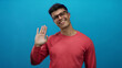 © Krakenimages.com - Smiling man in glasses and red sweater waving against blue background showing warm greeting.