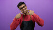 © Krakenimages.com - Young man with glasses smiling and pointing at his teeth against a purple background wearing a casual red sweater and denim apron.
