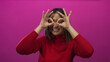 © Krakenimages.com - Chinese woman in red sweater making glasses gesture with her hands against a vivid pink background, smiling joyfully in an isolated playful setting.