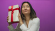 © Krakenimages.com - Chinese woman holding a gift box with a red ribbon smiling against an isolated purple background.