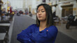 © Krakenimages.com - Woman standing on city street with arms crossed, wearing a blue blouse, showing a thoughtful expression amid an urban outdoor setting during daylight.