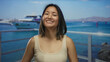 © Krakenimages.com - Young woman smiling by the sea with a boat in the background, capturing a joyful moment at an outdoor port location with a clear blue sky and water view.