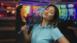 © Krakenimages.com - Young chinese woman holding a tennis racket confidently in a vibrant indoor casino, surrounded by colorful slot machines and lively atmosphere.