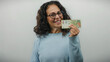 © Krakenimages.com - Woman smiling holds argentine pesos in casual sweater against a white background highlighting middle age and financial concepts.