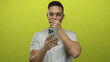 © Krakenimages.com - Young man with smartphone in hand looks surprised against bright yellow background, captivated by something on screen.