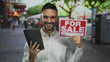 © Krakenimages.com - Hispanic man smiling with tablet and for sale sign standing outdoors in bustling urban street