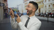 © Krakenimages.com - Hispanic man in white shirt and tie expressively pointing in an urban city street setting with blurred buildings and people in the background, wearing glasses and appearing surprised.