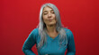 © Krakenimages.com - Senior woman with grey hair in blue sweater holding stomach appears uncomfortable against red background.