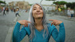 © Krakenimages.com - Senior woman with grey hair smiling and pointing at herself on a busy street outdoors wearing a blue sweater while people walk in the background