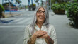 © Krakenimages.com - Senior grey-haired woman with tattoos smiling warmly on a sunny street, showcasing joy and positivity in an urban outdoor setting with trees lining the sidewalk.