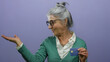 © Krakenimages.com - Senior woman with grey hair holding a credit card and gesturing something on an isolated purple background depicts finance concept