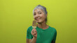 © Krakenimages.com - Senior woman enjoying ice cream against a vibrant yellow background, showcasing happiness and indulgence with tattoos and grey hair adding character.