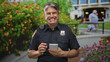 © Krakenimages.com - Police officer man writing in notepad at building entrance, smiling and holding radio while showing badge; friendly community service.