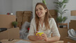 © Krakenimages.com - Caucasian woman smiles while holding yellow mug among cardboard boxes and potted plant inside building; comfort.
