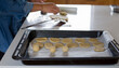© Marian - Asadera o placa para horno con papel manteca donde reposan galletitas caseras sobre la mesada de la cocina, detras se ven las manos amasando