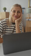 © Krakenimages.com - Woman resting hand on chin at home office desk with laptop and stacked moving boxes; calm reflection.