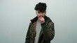 © Krakenimages.com - Young man with black hair making a vigilant gesture in front of a white wall background wearing a jacket displaying a curious expression indicating watchfulness and focus.