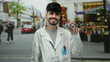 © Krakenimages.com - Young man in white coat smiling and holding optical tool outdoors on an urban street with shops and cars in background.