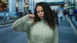 © Krakenimages.com - Woman with curly hair wearing sweater makes thumb down gesture on busy city street expressing disapproval outdoors in blurred urban background.