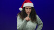 © Krakenimages.com - Hispanic woman in santa hat and sweater pointing finger in warning against a blue background, conveying disapproval and holiday authority.