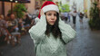 © Krakenimages.com - Woman wearing santa hat feeling stressed on cafe terrace with bustling street background suggests holiday overwhelm and urban life contrast.