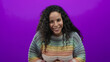 © Krakenimages.com - Woman smiling in rainbow sweater over vibrant purple wall, portraying joyful mood and isolated background with curly hair.