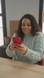 © Krakenimages.com - Woman smiling at phone in bright living room surrounded by moving boxes, wearing cozy sweater with happiness and surprise, reflecting new beginnings and communication joy.