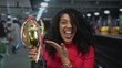 © Krakenimages.com - Smiling african american woman in red top holds golden trophy and raises fist at train station platform; triumph.