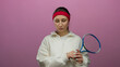 © Krakenimages.com - Woman holding tennis racket in white attire against pink background looking thoughtful with headband displaying contemplation over isolated setting involving sports equipment.