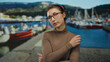 © Krakenimages.com - Woman pondering outdoor near a port with boats in the background, wearing glasses and brown top, with mountains visible, suggesting a thoughtful moment.