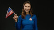 © Krakenimages.com - Young woman holding usa flag and wearing vote badge against an isolated black background, symbolizing american civic engagement and patriotism.
