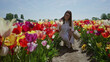 © Krakenimages.com - Woman enjoying colorful tulip field in lisse, netherlands, holding basket and bending to smell flowers under sunny blue sky, surrounded by vibrant blooms.