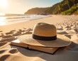 © Buka - Sun hat rests atop an open book, on sandy beach, ocean in background